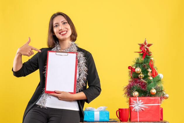 生活圣诞气氛 微笑的美丽女士站在办公室 指着黄色的办公室文件人指着成人
