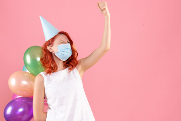 成人正面图：年轻女性手持彩色气球 戴着粉色的无菌面具面具粉色彩色