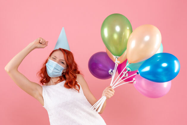 气球正面图：年轻女性手持彩色气球 戴着粉色的无菌面具年轻女性举行庆祝