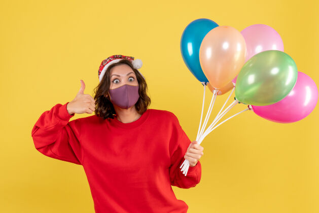 圣诞节正面图年轻女性拿着气球 戴着黄色的无菌面具前面年轻女性黄色