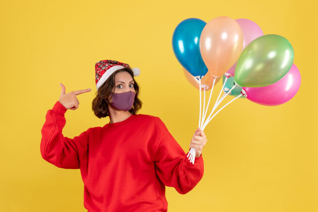 黄色正面图年轻女性拿着气球 戴着黄色的无菌面具圣诞节年轻女性面具