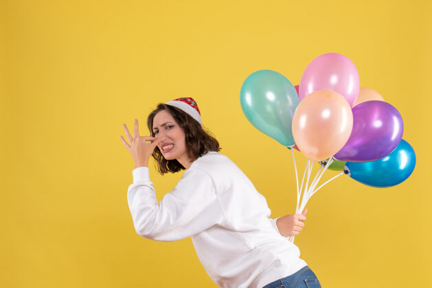 庆祝正面图年轻女性隐藏在黄色背景上的彩色气球新年圣诞彩色节日女性情感生日颜色年