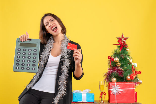 肖像圣诞节的心情与情感美丽的女士站在办公室里 拿着计算器银行卡在黄色的办公室心情美丽的女士黑发
