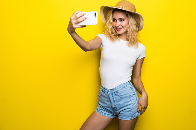 笑照片中兴奋的女人一边自拍一边玩得很开心 隔离在黄色的墙上微笑漂亮20多岁