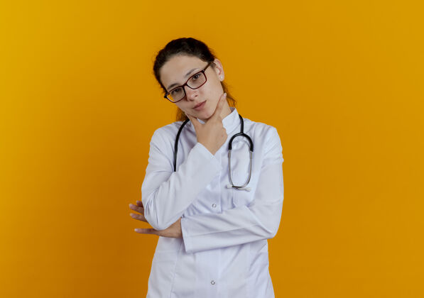 橙色看上去年轻的女医生穿着医用长袍 戴着眼镜听诊器 把下巴孤立起来年轻人成年人女人