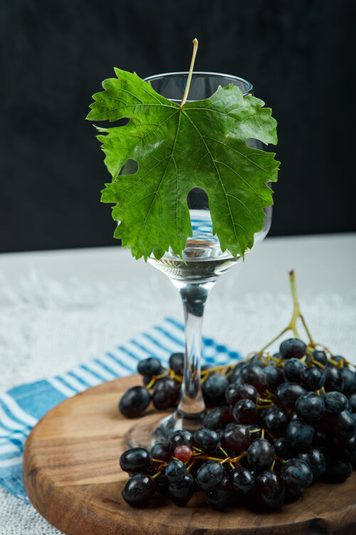 桌布一束黑葡萄和一杯白桌子上有叶子的葡萄酒高质量的照片盘子玻璃新鲜的