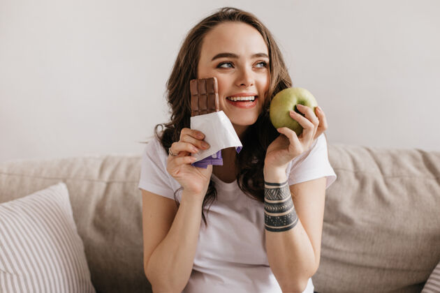 成人一个快乐的黑发年轻女子拿着绿苹果和甜牛奶巧克力的特写镜头房子触摸休闲
