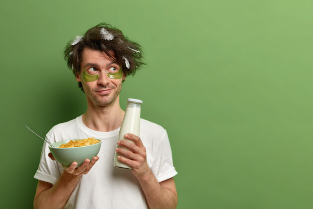 个人年轻人的水平镜头早上醒来 拿着一碗麦片和牛奶当早餐 有健康的营养或饮食 坚持节食 戴着胶原蛋白贴片 隔离在绿色的墙上立场垫补丁