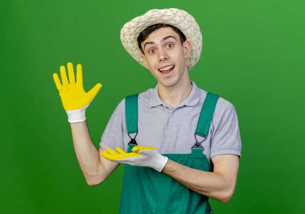 复制惊讶的年轻男园丁戴着园艺帽子和手套点在空手孤立的绿色背景与复制空间惊喜手套帽子