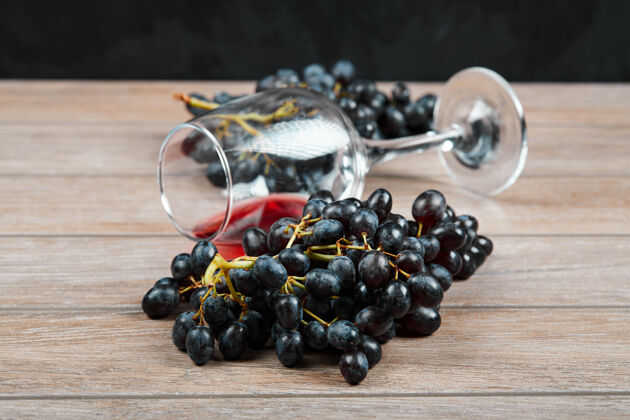 木材一束黑葡萄和一杯葡萄酒在木制背景上高质量的照片自然葡萄酒杯