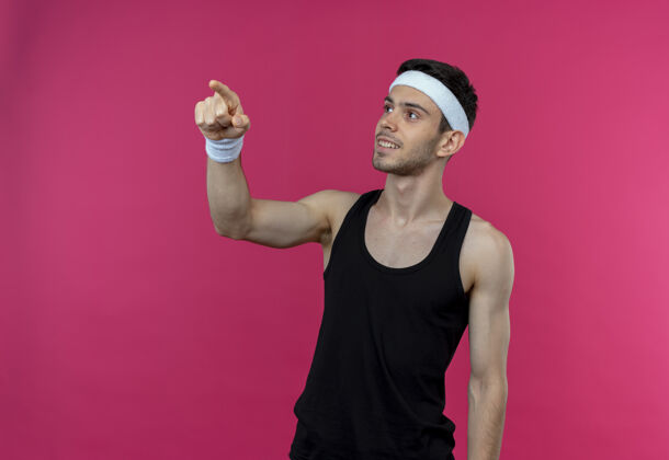 目录戴着头巾的年轻运动型男子一边看一边用食指指着站在粉色背景上微笑的东西站着头带年轻