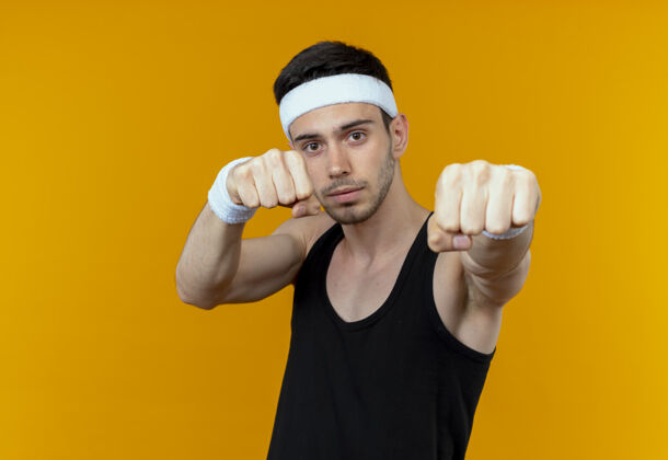 年轻戴着头巾的年轻运动型男子握紧拳头 站在橙色背景上向镜头展示运动站立握紧