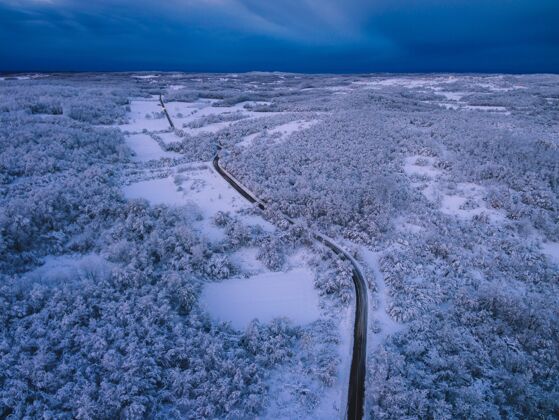 乡村在傍晚的多云天空下 鸟瞰一条被白雪覆盖的树木环绕的道路天空霜冻嗡嗡声