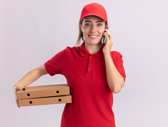感觉身着制服 面带微笑的年轻漂亮女送货员在电话中交谈 并在白墙上孤立地拿着比萨饼盒电话盒子公民