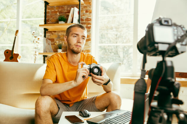 现场年轻的白人男性博主 带着专业设备 在家里录制摄像机的视频评论博客 视频博客 视频博客关于照片或技术新颖性的男人制作视频博客或直播流直播内容虚拟博客