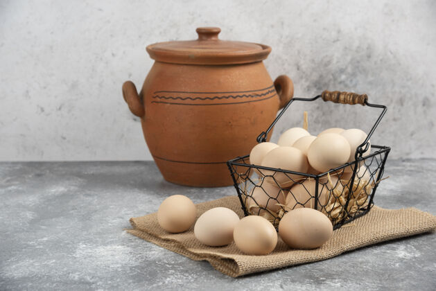 鸡蛋金属篮生鸡蛋和古董花瓶在大理石表面生的贝壳美味
