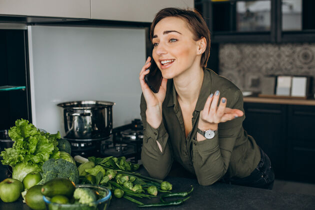 营养女人在厨房打电话 用绿色蔬菜做饭移动年轻新鲜