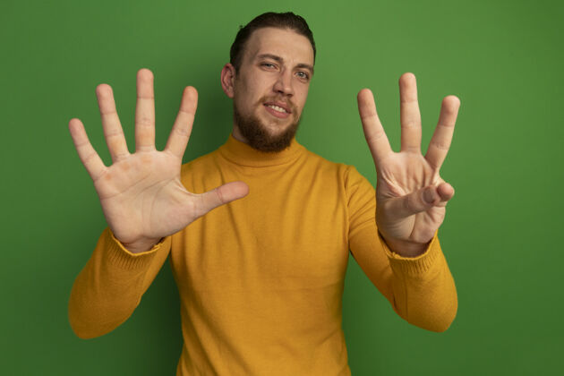 表情自信帅气的金发男人在绿墙上用八个手指做手势站感觉人