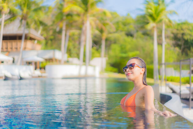 年轻人肖像美丽的亚洲年轻女子放松微笑休闲周围的室外游泳池在度假酒店海景女孩游泳池健康