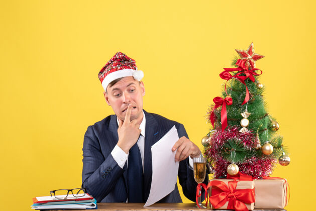 办公室前视图激动的男子坐在圣诞树附近的桌子上 呈现黄色背景商务树附近