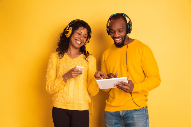 表情年轻感性的非裔美国人 穿着黄色背景的明亮休闲服美丽的情侣人类情感的概念 面部表情 关系 广告使用平板电脑和智能手机美国年轻成人