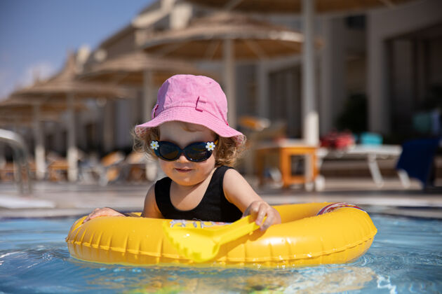 游泳池戴着帽子和太阳镜的可爱小女孩坐在游泳池里玩游泳休息游泳圈