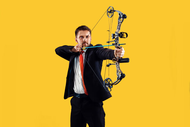注意商人用弓箭瞄准目标 孤立在黄色工作室背景上商业 目标 挑战 竞争 成就理念弓控制年轻