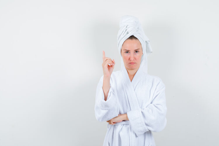 卷发画像中的年轻女子指着白色浴衣 毛巾和期待犹豫的前视图成人尖肖像