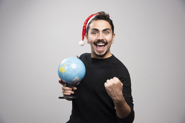 年轻戴着圣诞老人帽子拿着地球仪的快乐男人介绍时尚英俊
