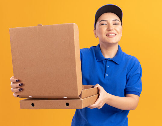 欢呼身着蓝色制服 头戴鸭舌帽 手持披萨盒 打开披萨盒 面带微笑 站在橙色墙壁上的快乐年轻女送货员女人快乐帽子