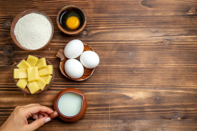 生的俯视整个生鸡蛋与面粉牛奶和奶酪在棕色的桌子上鸡蛋面团面粉粉尘产品顶部鸡蛋牛奶