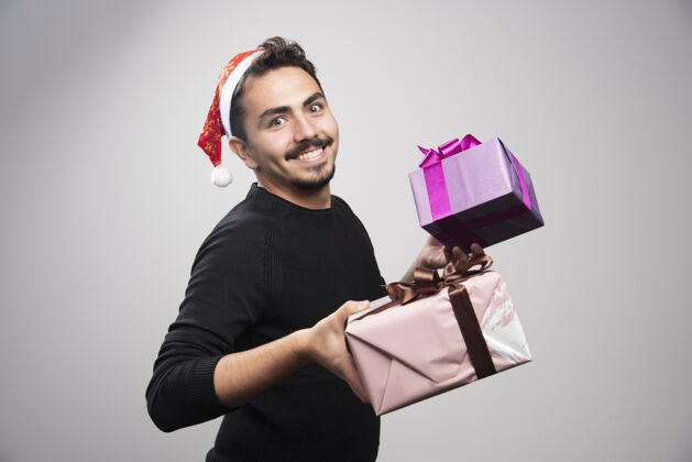 肖像一个年轻人拿着礼品盒在灰色的墙上模特男人礼物