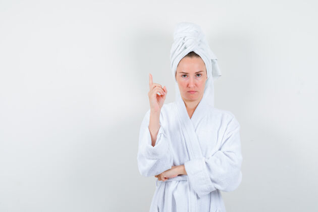 卷发画像中的年轻女子指着白色浴衣 毛巾和期待犹豫的前视图成人尖肖像