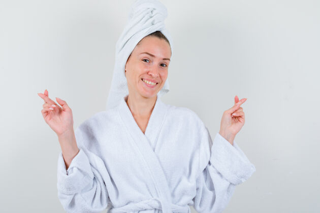 漂亮年轻的女士在白色浴衣 毛巾和手指交叉 看起来很高兴前视图头部前面护理