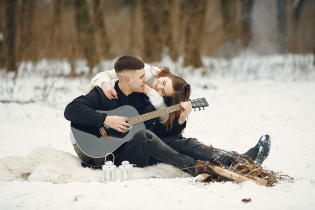 白色一对夫妇坐在雪林中的生活方式照片人们在户外度过寒假一对夫妇带着吉他人肖像在一起