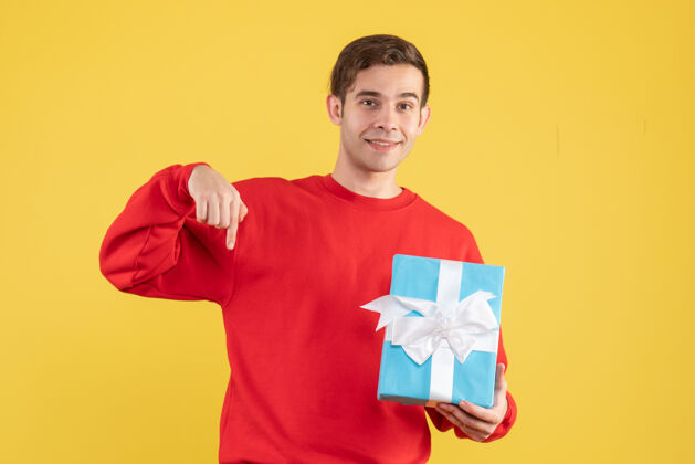 蓝色正面图：穿着红色毛衣的年轻人拿着黄色背景的蓝色礼品盒背景肖像年轻人