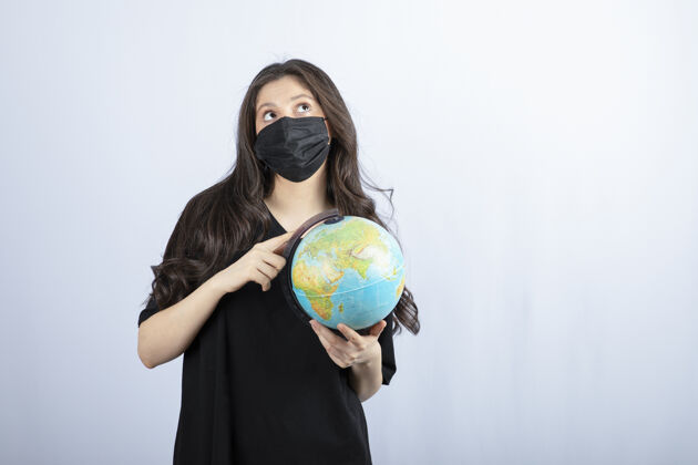 青少年戴着医用面具的黑发女人拿着世界地球仪学生年轻女士