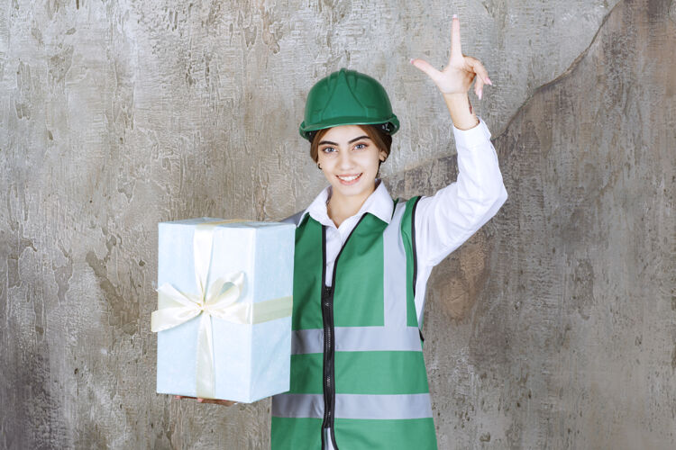 礼物身着绿色制服 头戴安全帽的女工程师手拿蓝色礼盒 有个好主意礼品盒注意关心
