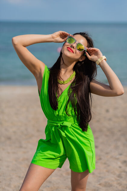 度假时尚户外夏日肖像美丽的年轻黑发美女戴着凉爽的太阳镜在阳光明媚的热带海滩上摆姿势天空优雅时尚