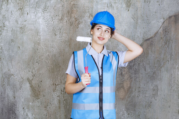 方式身穿蓝色制服 头戴钢盔的女工程师 手持修边滚筒进行绘画 思考和规划姿势方法修理