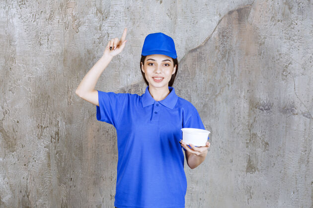 食物穿着蓝色制服的女服务人员拿着一个塑料碗 看上去很困惑 很有想法 或者有个好主意外卖姿势送货