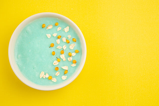 陶器俯视图蓝色冰甜点在盘子里放在一张黄色的牛奶麦片色的桌子上餐具水容器