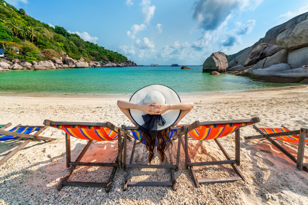夏天戴着帽子的女人坐在美丽的热带海滩的椅子上在南苑岛的热带海滩上放松的女人热带日光浴床度假