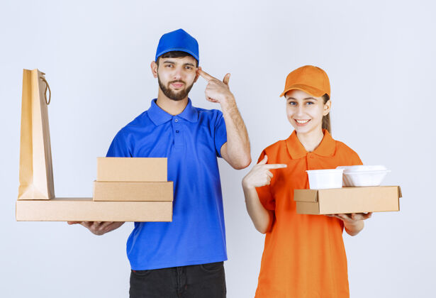 员工穿着蓝黄制服的快递员男孩和女孩拿着纸板外卖盒和购物包 看上去很困惑 在思考新的想法送货男性计划