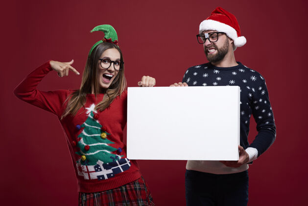 圣诞节穿着奇怪圣诞服装的年轻夫妇手里拿着白纸眼镜微笑怪人