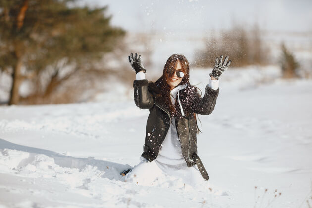 年轻穿黑夹克的女人的特写照片雪天站在森林里的女人白色女孩时尚