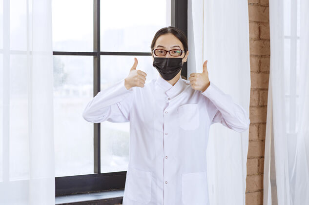 感染戴着黑面具和眼镜的医生站在窗边 展示着享受的标志女性协议预防
