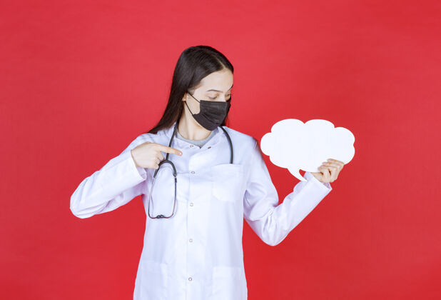 医院女医生带着听诊器 戴着黑色面罩 手里拿着一张云状的空白问讯台指南预防项目