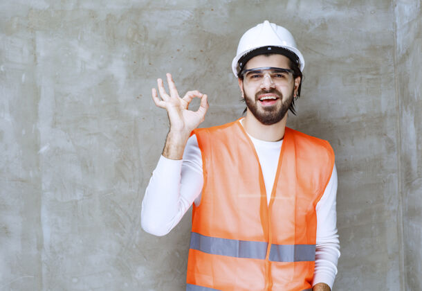 员工戴着白色头盔和护目镜的工程师 手上有“ok”的手势成功成人服装