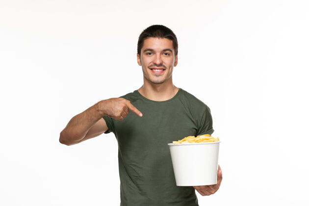 享受正面图身着绿色t恤的年轻男子拿着篮子和土豆在白色的墙上孤独地享受电影电影院观点微笑年轻的男性